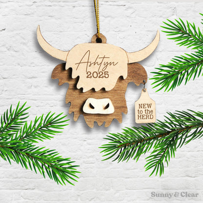 Wooden ornament shaped like a highland cow with engraved text, hanging on a branch.