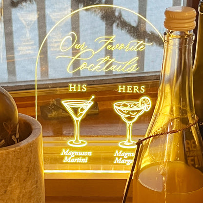 Decorative light sign with 'Our Favorite Cocktails' and cocktail illustrations, placed on a surface.