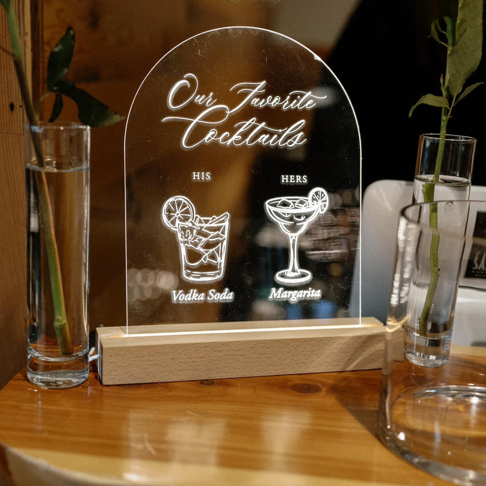 Decorative sign with 'Our Favorite Cocktails' on a wooden stand, flanked by two glasses of water.