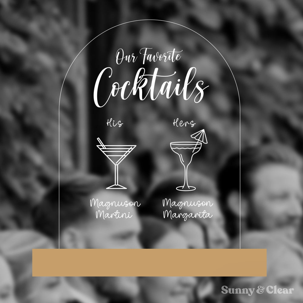 Acrylic sign with cocktail illustrations and text 'Our Favorite Cocktails' on a blurred background.
